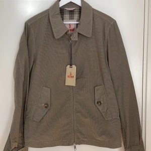  Baracuta vår/sommar jacka - Klassisk Baracuta jacka med krage. Ofodrad, rutigt mönster på insidan. Regular fit. Made in Italy. Justerbar i sidorna. Oanvänd.