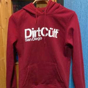 Dirtcult hoodie - Använd mörkröd hoddie och tvättad ett par gånger. Den är i fint skick. Det finns en liten fläck vid vä fickan, se bild 3. Säljer den för det är inte riktigt min färg   Köpare betalar frakt 