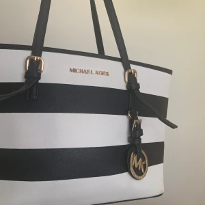 Michael Kors väska! - Fint använd väska, jättefint skick så som ny! Vit och svart randig, ett litet fack med dragkedja och 2 små fack också, alla 3 på insidan, inga på utsidan! ÄKTA!!!