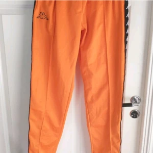 Kappa byxor - Orangea byxor från Kappa med gömd snörning i midjan och knappar längs benen. Dom är i storlek XL men passar perfekt på mig som är M.