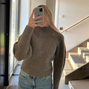 Stickad tröja - Jätte fin stickad tröja med hög krage och ”ballong ärmar”. Funkar utmärkt vid både finare tillfällen och som mysig varm tröja. Tröjans material är delvis alpaca, delvis ull och delvis polyester. Storlek XS. Färgen är en fin kall brun.