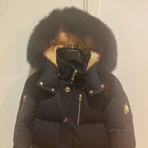 Moose knu kles Storlek small (S) - Svart moose knu kles jacka i jättebra skick. Har endast haft den sen vintern 2020 men ser nästan helt ny ut. Svart päls på luvan och guldiga detaljer. Kemtvättas innan köp. 