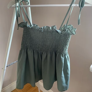 Smockat grönt linne - Ett grönt smockat linne med justerbara axelband. Köpt utomlands så storlek saknas, däremot är den väldigt spänstig i materialet då den är smockad samt justerbara knytband så passar 34-38, mått kan skickas. Utan anmärkningar. Varan kan även fraktas 📦