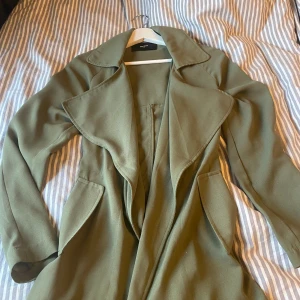 Vårkappa - Vår/sommar kappa i mörkgrön, väldigt tunn och lätt. Det finns ett band till jackan man har runt midjan men de kom ej med på bilden, kan Skixka fler bilder om det önskans