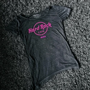Hard Rock cafe Ibiza - N Hard Rock Cafe T-shirt Ibiza orginal. Lite längre på ena sidan ner till för att man ska kunna knyta den i midjan. Tunt tygg. Rosa tryck. Fattas en liten pärla i trycket. Annars hel och ren.