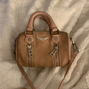 Zadig sunny nano väska  - Säljer nu min fina Zadig väska, den är i en super fin smutsrosa/ljusrosa färg! Säljer den nu för bra pris då jag inte får användning för den! Köpte den begangnad på shpock, defekterna på väskan är då baksidan och delar på framsidan där mörka tyger har färgat av sig, samt små defekter inuti. Men det går säkert att få bort med nån slags mocka tvätt.    Priset är sänkbart vid snabb affär! Dustbag ingår ej!