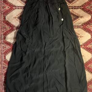 Lång svart kjol med två knappar och slit på sidan. 