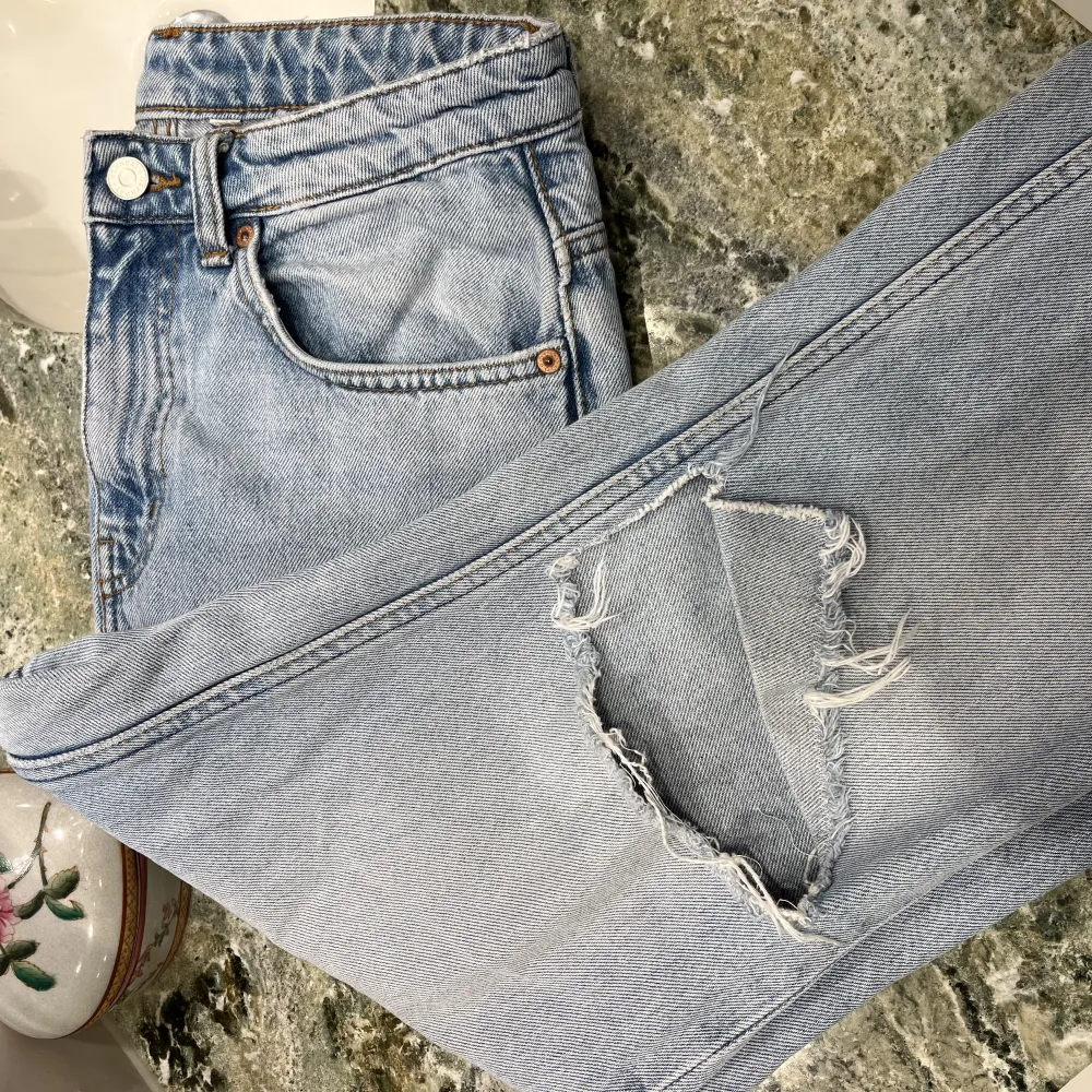 Straight jeans från Weekday i modellen VOYAGE. Superfin ljusblå urtvättad färg med ett egetklippt hål i knät som en fin detalj. Fint skick. Storlek 36. Skriv för fler bilder!. Jeans & Byxor.