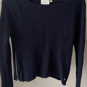 Stickad tröja - En mörkblå stickad tröja med silvriga dragkedjor på båda sidor. Går ganska långt ner på axlarna och är ganska bred längst kroppen. Köpt för 130kr. Ser lite använd ut då den är köpt secondhand men annars är den i bra skick.
