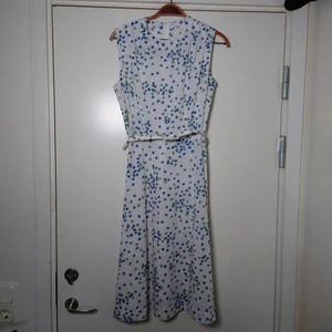 Vintageklänning  - Vit äldre vintageklänning med mönster i blått och grönt. Skärp i midjan som kan tas av. Dragkedja i ryggen. Ingen storleksmärkning men är som en M🌻