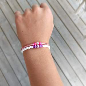 Två hemma gjorda armband som man kan ha som kompisarmband det får man bestämma själv. Ett armband är lila och vit och ett är rosa.