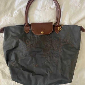 Väska - Mörkblå/grå väska med bruna remmar, champagnefärgade detaljer och guldknappar samt guld dragkedja. Väskan har Longchamp märket men är en fejk, minns inte vart den köptes men kopian är väldigt övertygande. Nyskick!
