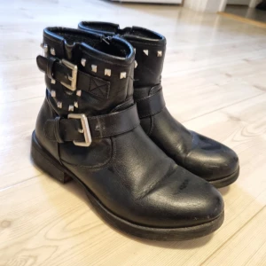 Svarta boots med nitar stl. 38 - Svarta boots från DinSko med nitar och spännen på sidorna. Fodrade. Storlek 38. De har några år på nacken så därför finns det lite märken på sulorna som ej går bort.