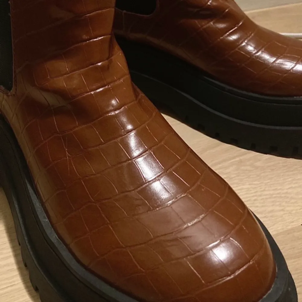 Krokodilmönstrade bruna chelsea boots med platå, nya och oanvända. Nypris 587kr, helt slutsålda. Frakt tillkommer eller så kan de hämtas i Sundbyberg :). Skor.