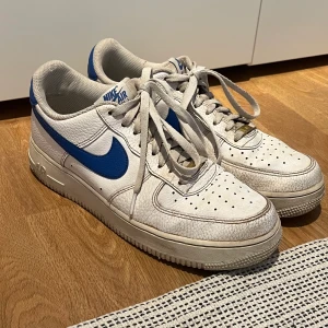 Nike Air Force 1 Low White Royal Blue Strl 42,5 - Vit/Blå Nike Air Force 1 i strl 42,5. Varsamt använda (har haft i crease-skydd i dem). Dock lite slitna inuti på höger sko men det syns ej när dem är på. Pris kan diskuteras.