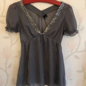 Glittrig top - Genomskinlig grå skimrig top med paljetter på v-rigningen.