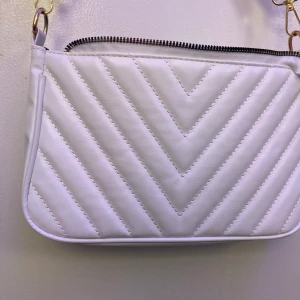 vit handväska i läderimitation  - Väskan nästan som ny och är bara använd två gånger. Det är en axelremsväskan men går även att byta till ett kortare band