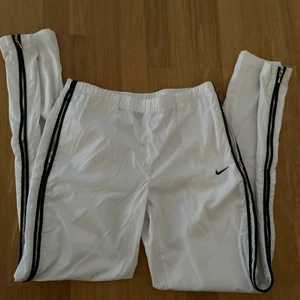 Nike Trackpants - Säljer dessa sjukt fina vita trackpants från nike med svarta detaljer längst sidan. Köpta för längesen men i nyskick då dem är använda max 5gånger. Säljer också då dem är försmå för mig tyvärr. Ser ut som att dem är midwaist ish. 