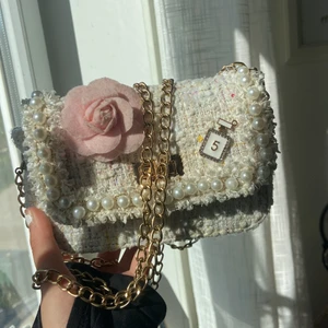  En vit ullfärgglad väska🤍 - En vit ullfärgglad väska med en blomma och en    liten pärla som är som en pärfym - detaljer       Och så har den en guldig kedja, och med en guldig knapp som man öppnar med❤️