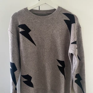 Grå stickad tröja med svarta blixtar. - En ny tröja (aldrig använd pga av beställt fel storlek).Väldigt fin och lite oversize i modellen. 
