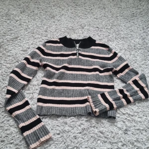 Långärmad stickad tröja - En randig tröja, med färgerna rosa, grå och svart. Den har en dragkedja vid halsen som funkar precis som den ska. Tröjan är från H&M och är helt i nyskick.