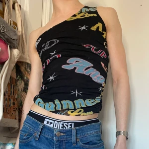 Svart enarmat linne mesh tryck text ruched rosa vit blå röd gul - Vintage svart enarmad meshtopp med tryck på fram och baksida av text som säger ”cupid”, ”angel”, ”wild” mm samt stjärnor 🪷⭐️ Älskaar detta linnet! Passar till allt eftersom det är svart med ändå så mycket roligare än ett vanligt svart linne <3