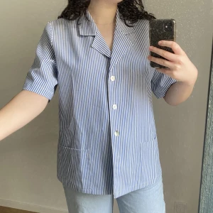 Randig skjorta - Blå vit randig kortärmad skjorta perfekt till våren och sommaren. Superfin till jeans eller uppknäppt med ett linne under. Köpt second hand och saknar märke. 