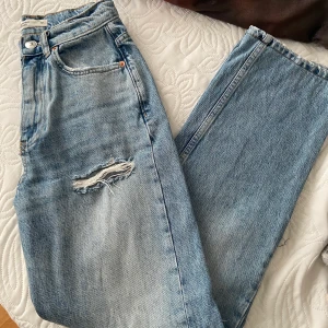 Blåa raka jeans - Blåa jeans med hål på knäna i modellen 90’s highwaisted straight leg från ginatricot. I storlek 32 men passar även strl 34. Uppsydda så passar mig i längd som är 158cm. 150kr + frakt
