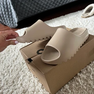 Yeezy slides - Säljer ett par yeezy slides i beige. Vet ej om de är äkta eller inte, jag köpte dom för  1 250kr och de ser väldigt äkta ut! Storlek 40 1/2 men jag har storlek 38. !helt oanvända!