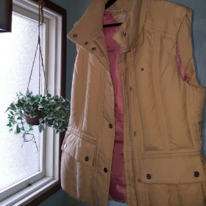  - Tommy Hilfiger damväst i stl XL. 4 fickor i fram och en på insidan, gömd huva i kragen. I princip oanvänt skick. Köparen står för frakt men kan också hämtas i Gävle/Sandviken