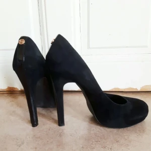  - Svarta klassiska pumps med hög stilettklack och platå i mocka, samt dekoration baktill. Endast använda vid två tillfällen, nyskick.