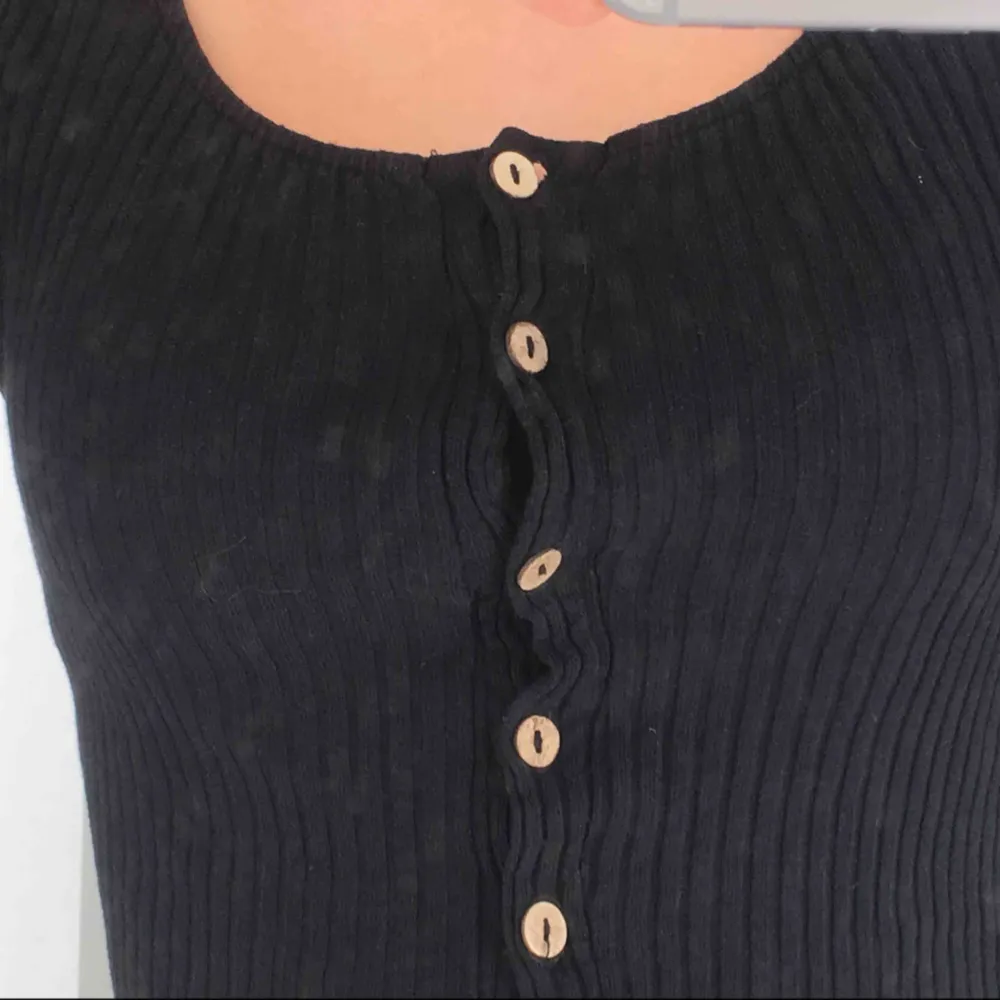 Svart långärmad tröja med knappar fram till som kan knäppas upp, kort på längden då man kanske behöver ha högmidjade jeans om man inte vill visa magen etc. (fläckig spegel). Toppar.