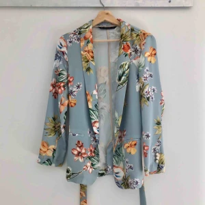  - Blommig blazer i mjukt silkesliknande material. Glansig. Knyts i midjan. Använd en gång. Slutsåld. Kan mötas upp eller skicka för 55kr.😊