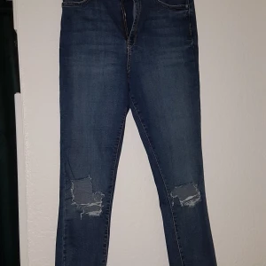 Blåa "slitna" jeans i strl 42 - Blåa jeans i sliten stil. Jeansen är i storlek 42 och har en bra passform.