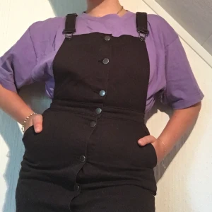 Svart hängselklänning - Svart hängselklänning i jeanstyg. Använd endast ett fåtal gånger, i nyskick. Frakten kan delas på.