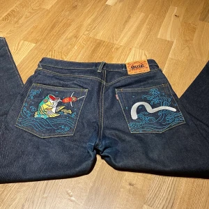 Evisu Jeans - Supercoola och trendiga Evisu byxor i väldigt fint skick! Snygga broderade mönster på bakfickorna och vanligt där fram, baggy fit. Storlek W:34 L:34 Köparen står för frakt!