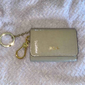  - Beige liten plånbok som fungerar att sätta på nyckelknippan och fästa på något. Superfin och smidig att ta med sig. Från Ralph Lauren