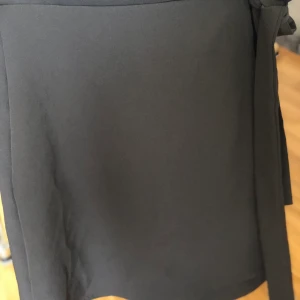 Svart kjol  - Svart kjol som du knyter vid sidan, aldrig använd men prislapp saknas. 