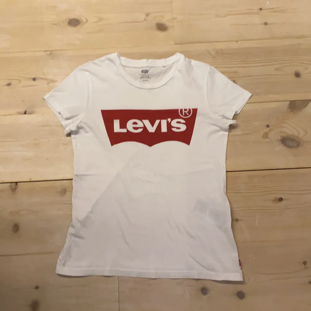 Vit fin mjuk Levis t-shirt med stort rött Levis märke fram.❤️🤍 Mycket bra skick, då den endast är använd ett fåtal gånger och tvättad kanske en eller två gånger. Material 100% bomull. (Säljer pga för liten och inte riktigt min stil längre). Jättefin, jättemjuk, bekväm och snygg till tex jeans. Storlek XS så på mig som är XS/S är den lite liten, men om man vill att den ska vara taight så är den ganska lagom. (Se hur den sitter på mig på första bilden). DM vid intresse/frågor/fler bilder.❣️(Det kan du göra här under där det står ”kontakta”). Avhämtning på Södermalm eller frakt till självbetalningspris.:). T-shirts.