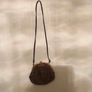  - En liten axelväska med naturligt slitage. Skinn är den gjord av.