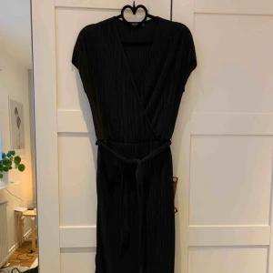  - Svart långklänning med slits i sidorna. På mig som är 1,65 går den strax ovanför fotknölarna. Plisserad men ändå stadigt tyg. Knytskärp i midjan. Figurnära men ändå skön passform. Aldrig använd.