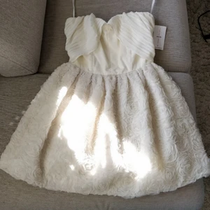 Cremevit festblåsa med fina detaljer - Fantastisk klänning från Jones & Jones. Oanvänd, lapparna är kvar. Storlek XS/size 8 (UK). Cremevit, med blommig underdel och tight ovandel med detaljer över bysten. Säljes pga för liten (så ifall ni har en likadan i storlek S/M, säg till!)