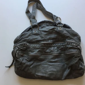  - Grön konstskinnsväska. Många fack och rymmer mycket. Väldigt mjuk i tyget och känns inte plastig.