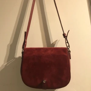  - Snygg röd väska med mockaimitation på framsidan. Kommer ej till användning. Fraktar endast, ej medräknat i pris. 