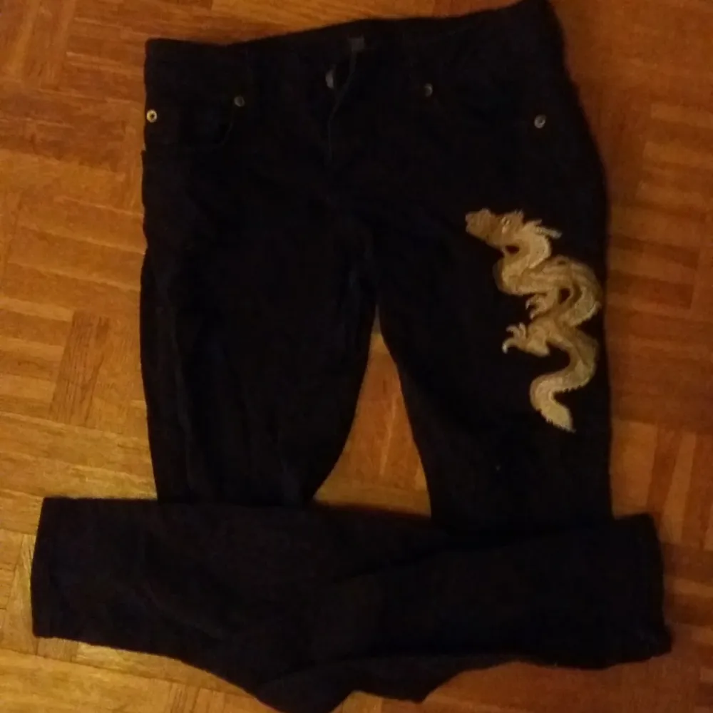 Svarta jeans med mode-slitningar och drakbroderi. 50kr. Stl 36.. Jeans & Byxor.
