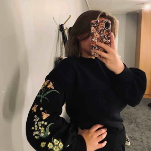  - Collegetröja med broderade blommor på ärmarna