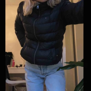  - Äkta Tommy Hilfiger dunjacka i modellen ”ESSENTIAL HOODED JACKET” , nypris 2275 kr, med avtagbar luva i förträffligt skick! Åsido från en minimal reva högst upp vid dragkedjan, men som inte syns över huvud taget :) 
