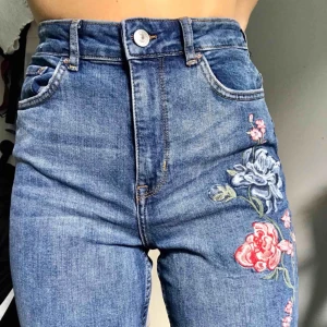  - Högmidjade jeans i mörkare tvätt. Gulliga broderade blommor längs vänstra benet. Något mindre i storleken, passar mig som vanligtvis har ca 36. Bra skick, inga hål eller fläckar.