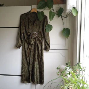 Zara - Klänning med knytdetalj - Klänning från Zara Woman i grönmönstrat syntetmaterial med spänne- och knytdetalj. Slits mitt fram, dragkedja i sidan. Oanvänd. OBS! Storlek S, men mer som en XS (framförallt över höfterna).