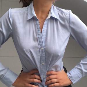 En ljusblå och vit, smalrandig skjorta från H&M. Superskönt material och snygg passform för kvinnor!
